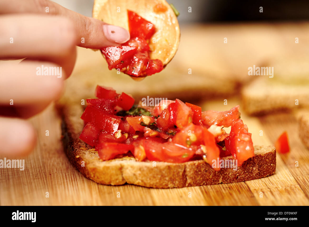 Closeup of cook's hands preparing tomato bruschettas on a wooden board Stock Photo