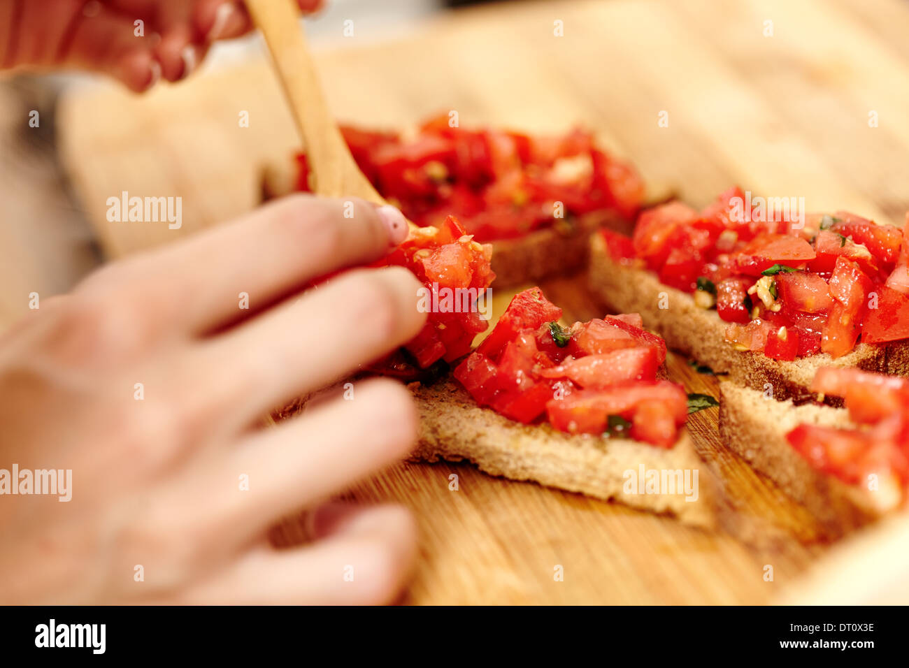 Closeup of cook's hands preparing tomato bruschettas on a wooden board Stock Photo