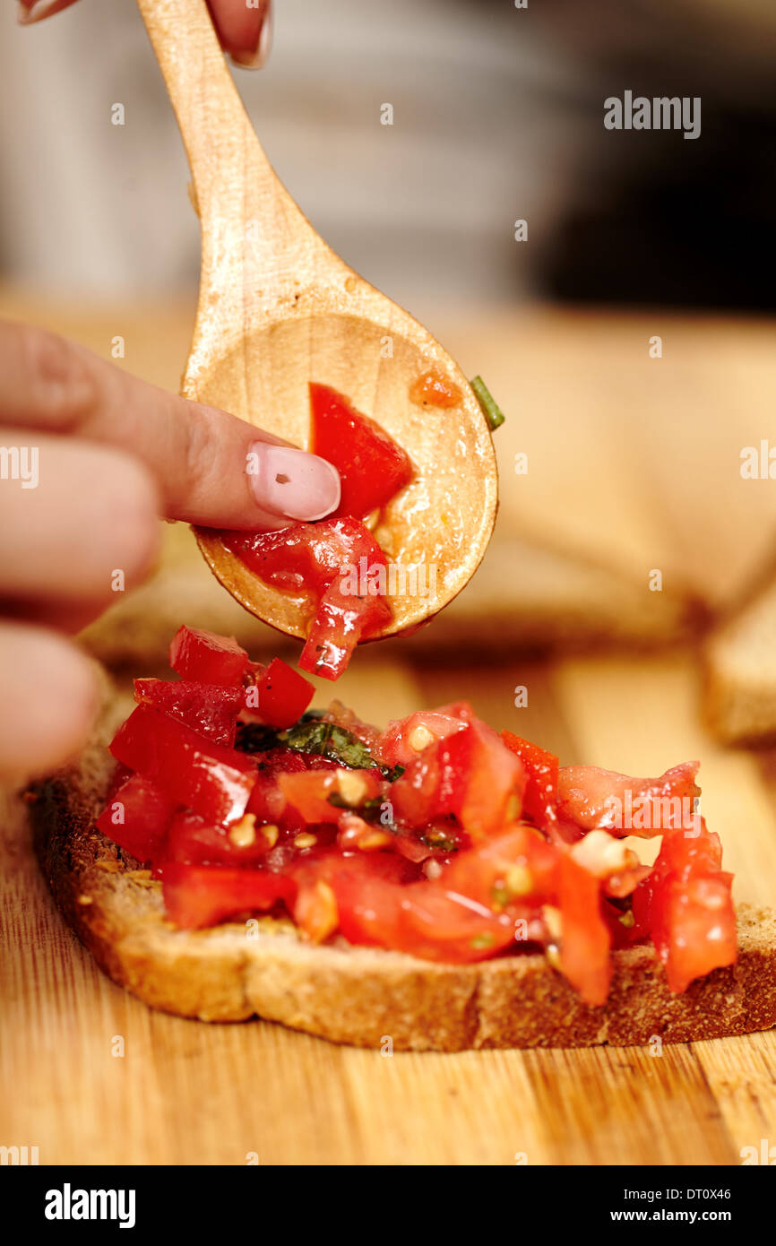 Closeup of cook's hands preparing tomato bruschettas on a wooden board Stock Photo