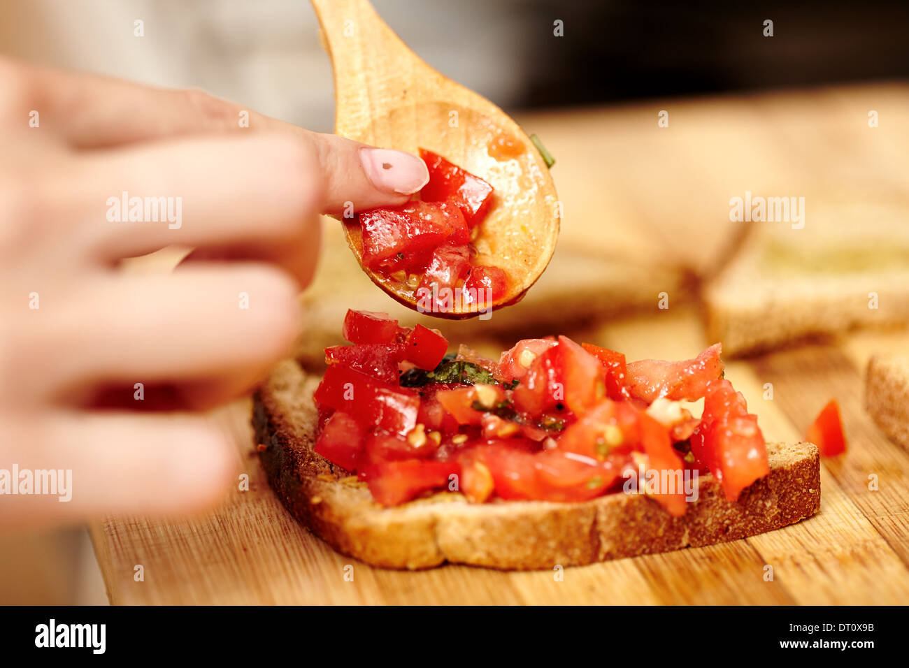 Closeup of cook's hands preparing tomato bruschettas on a wooden board Stock Photo