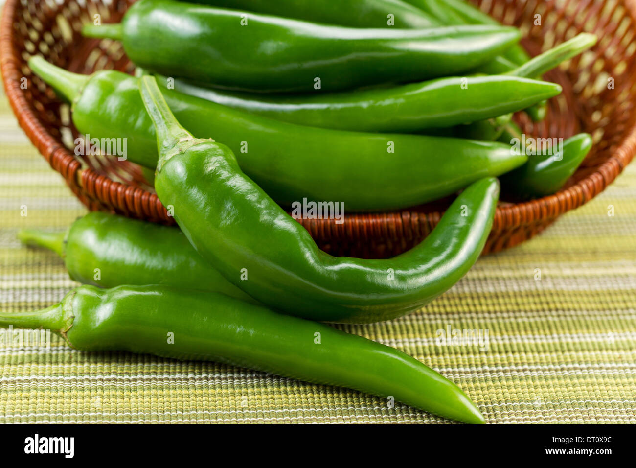 Closeup horizontal photo of fresh Korean Green Peppers falling out of basket with textured table cloth underneath Stock Photo