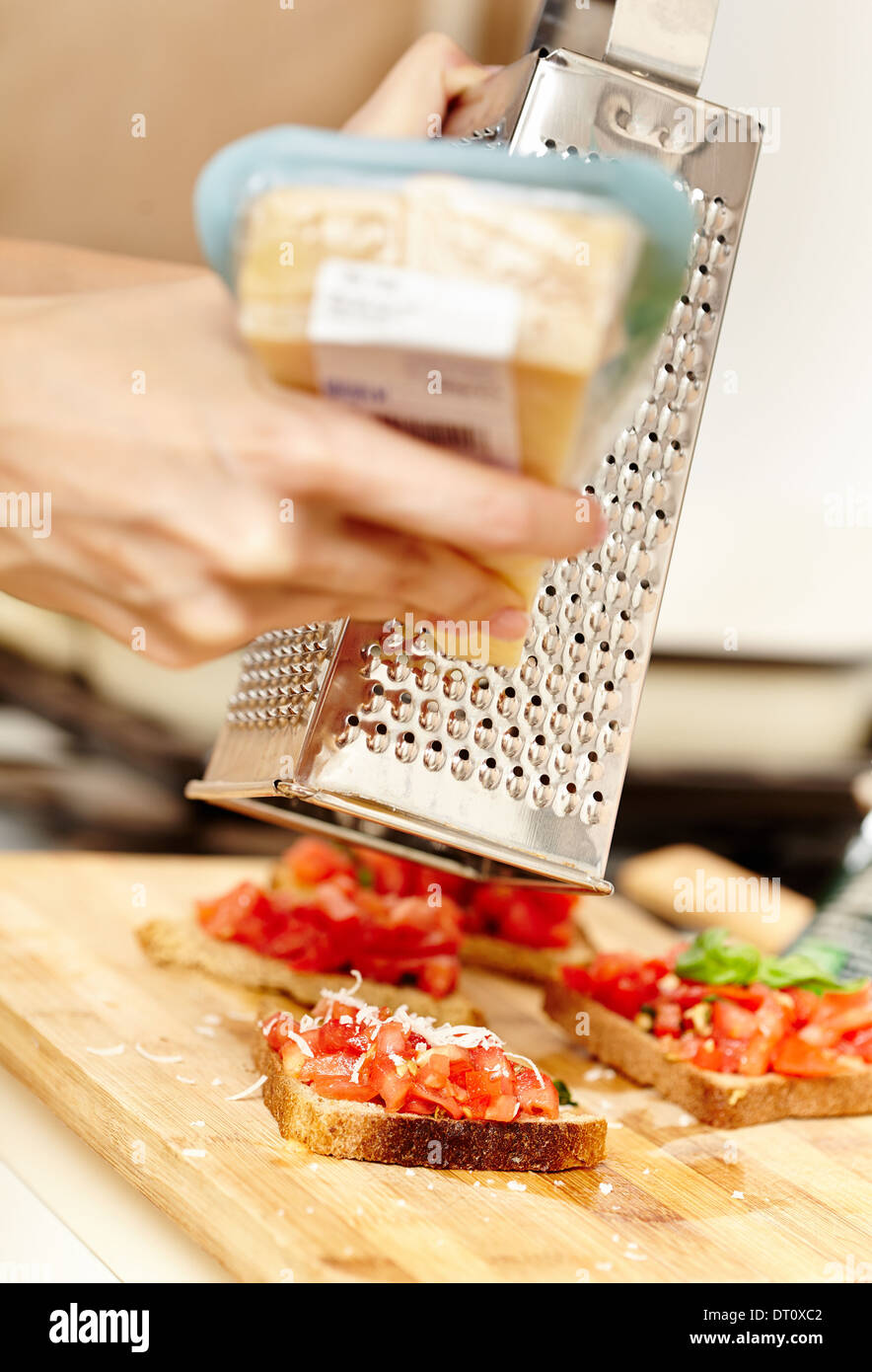 Closeup of cook's hands grating a lump of parmesan over tomato bruschettas, selective focus Stock Photo