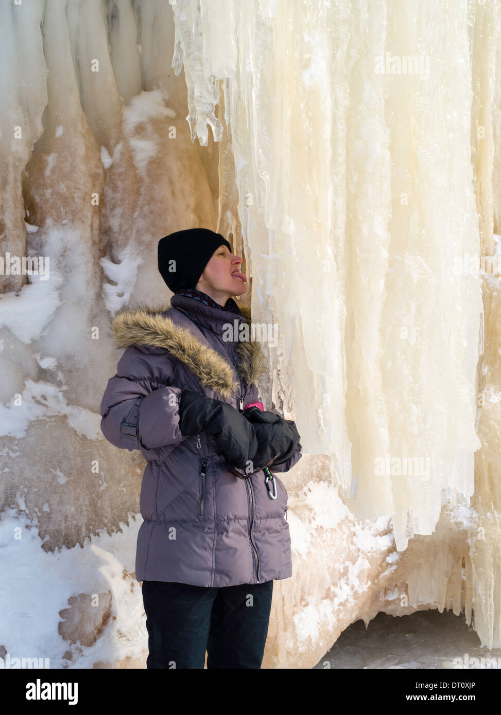A beautiful woman licks an ice stalactite at the Apostle Island Ice Caves, Makwike Bay, near Bayfield, Wisconsin, on a cold Feb Stock Photo