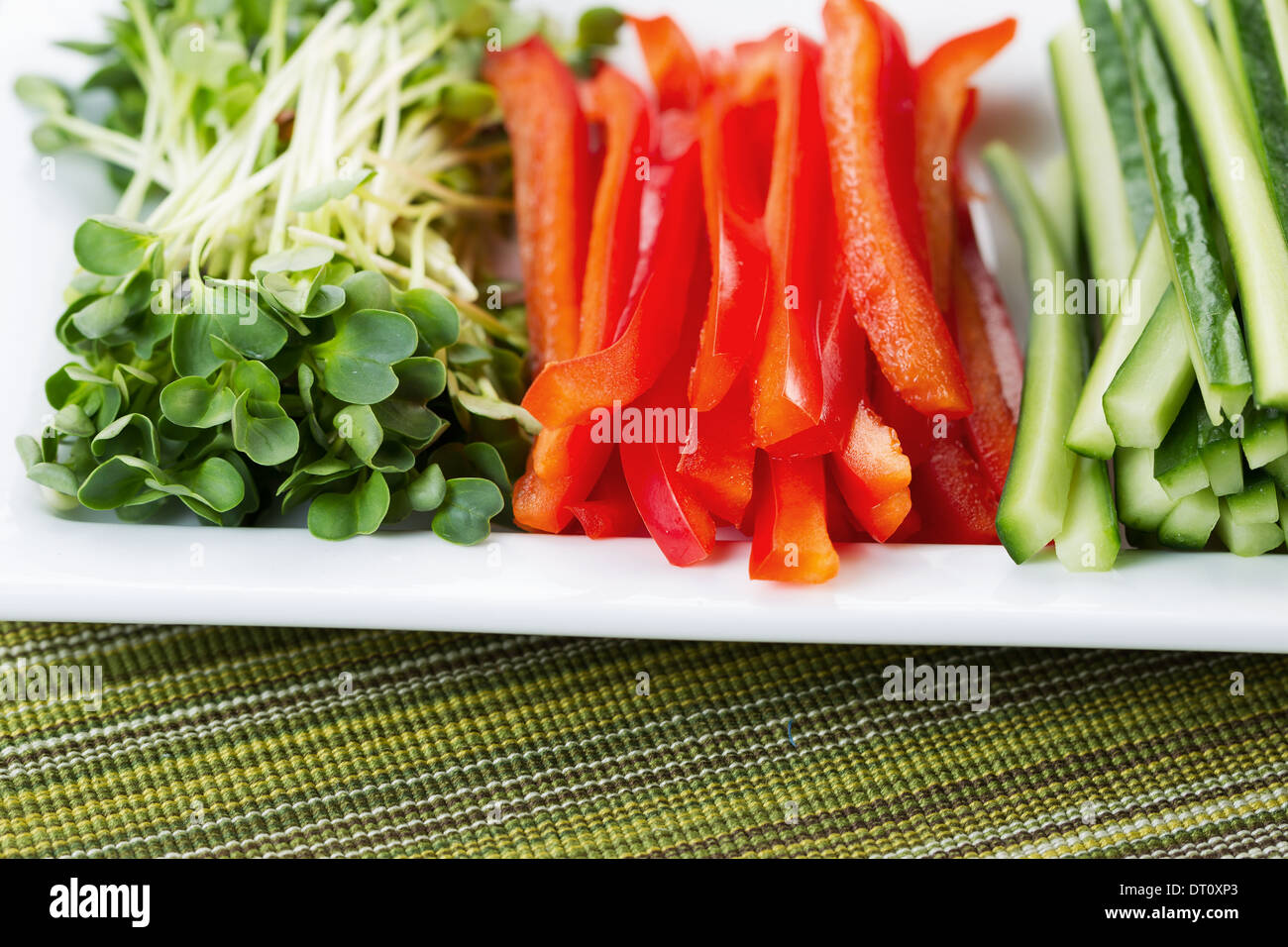Horizontal closeup photo of freshly sliced red peppers, placed in white plate, along with sliced cucumbers, and daikon radish Stock Photo