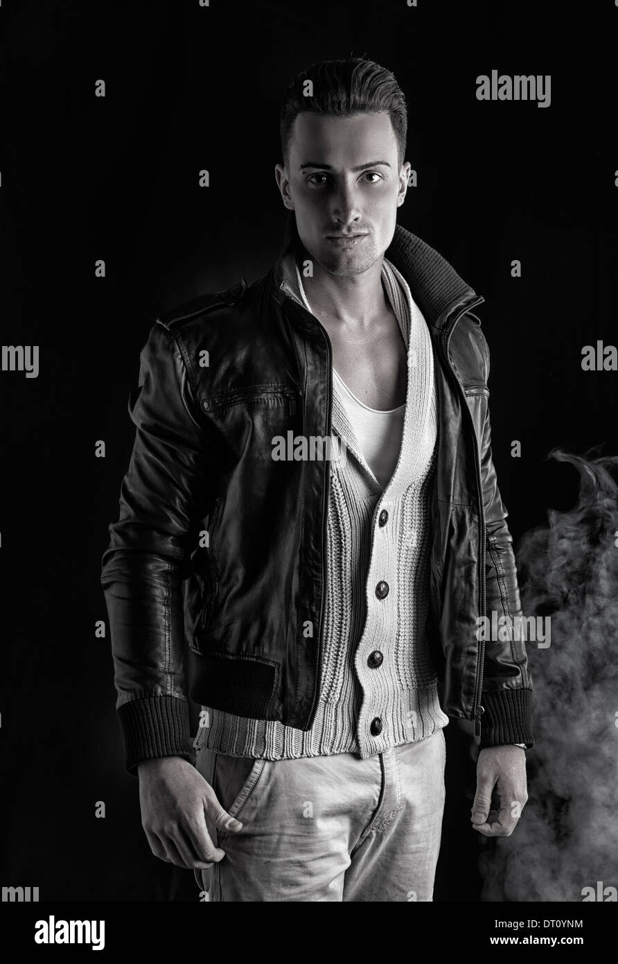 Attractive young man with white sweater and black leather jacket. Smoke and dark background. Stock Photo