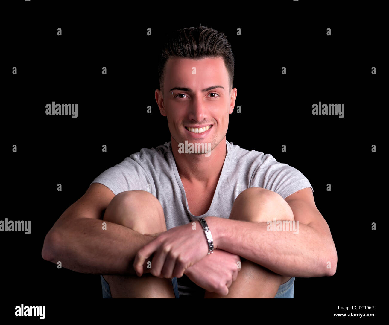 Attractive young man smiling, sitting and keeping his arms around his knees Stock Photo Alamy