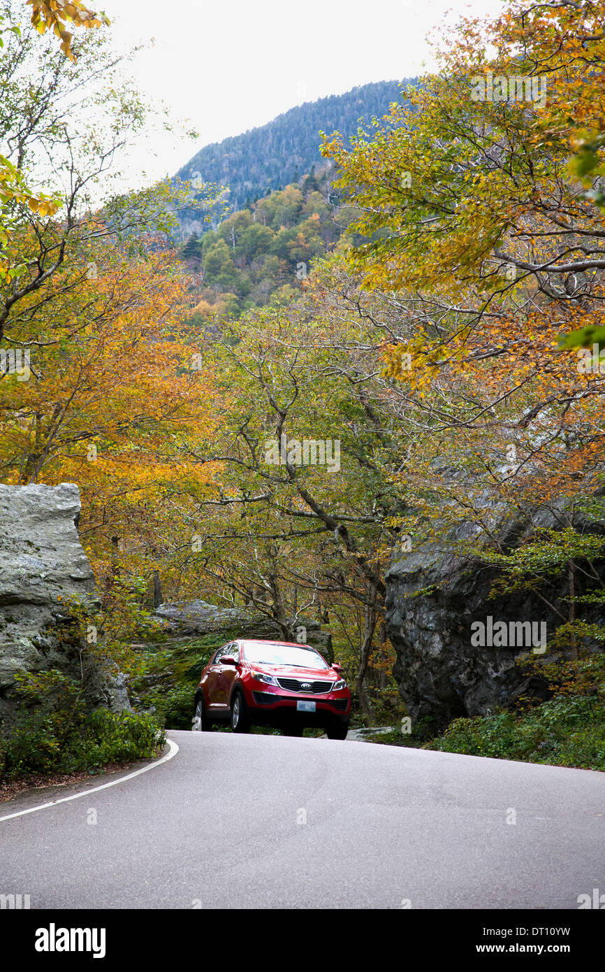 Red car approaches top of Smugglers' Notch (VT 108) through graceful trees on west side of road in Vermont's Green Mountains. Stock Photo