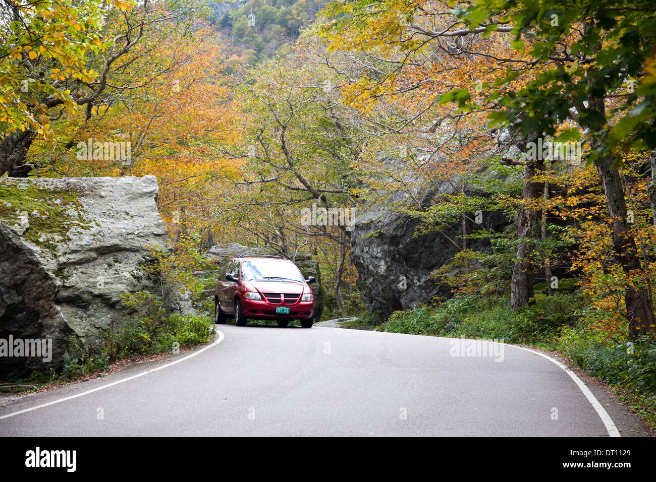 Red car approaches top of Smugglers' Notch (VT 108) through graceful trees on west side of road in Vermont's Green Mountains. Stock Photo