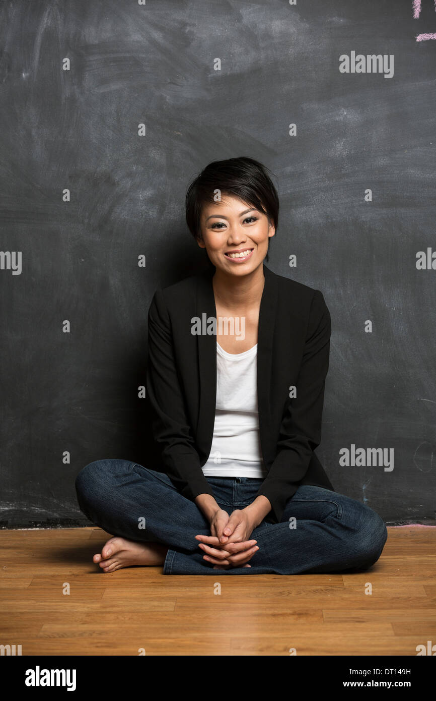 Happy Asian woman sitting in front of a chalk board. Stock Photo
