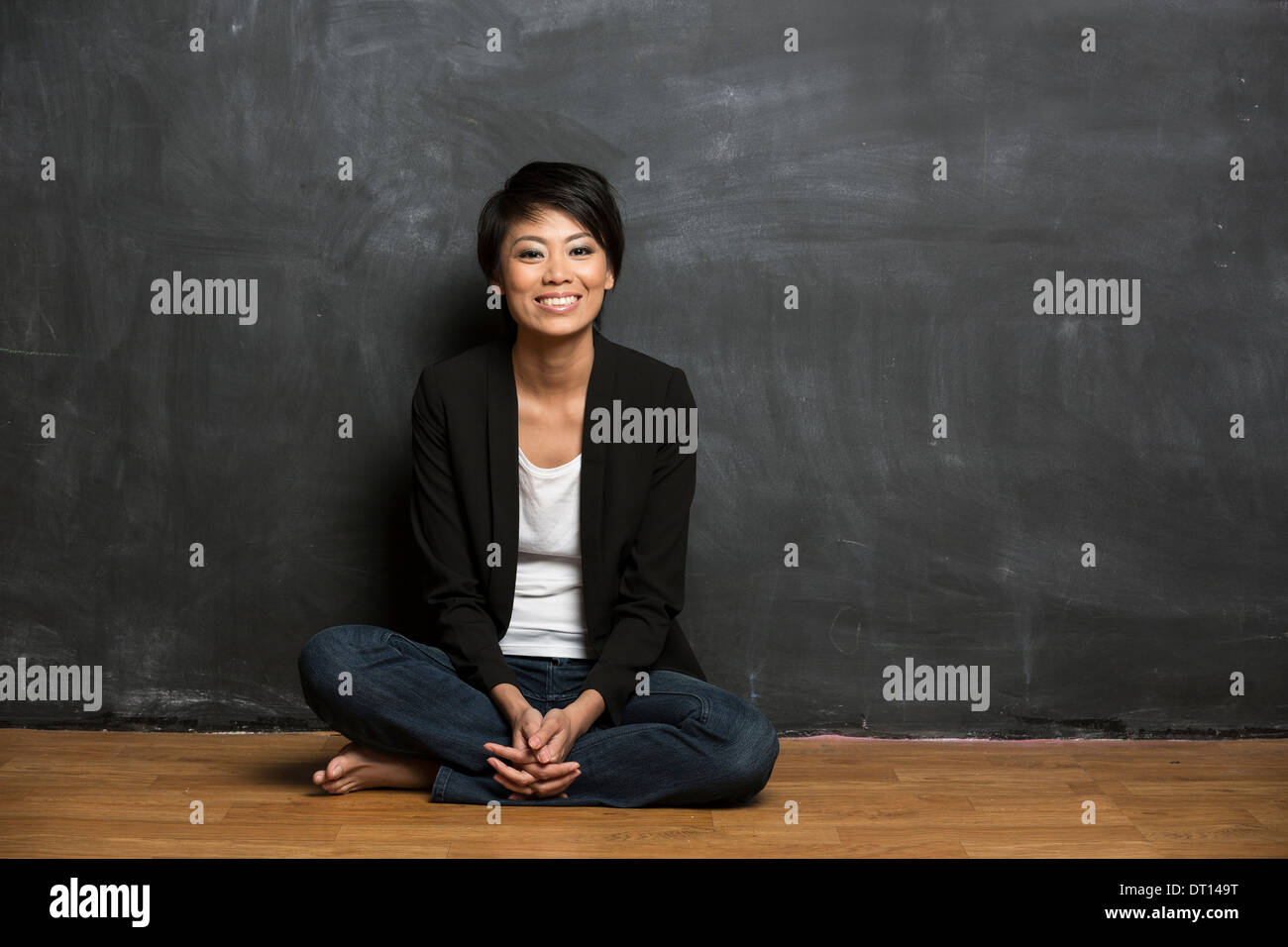 Happy Asian woman sitting in front of a chalk board. Stock Photo