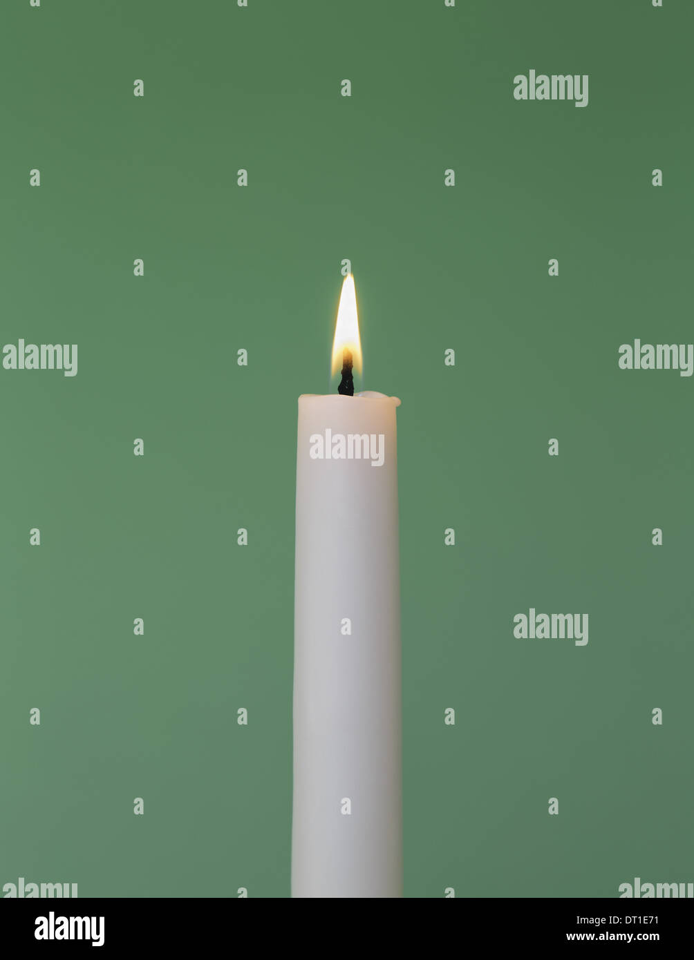 thin white wax candle with small lit flame Stock Photo