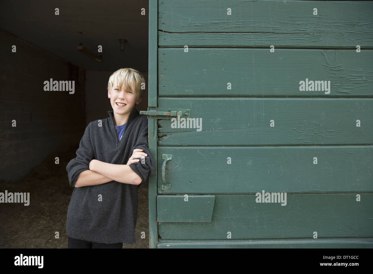 A boy leaning against a wooden barn door at an animal sanctuary Stock Photo