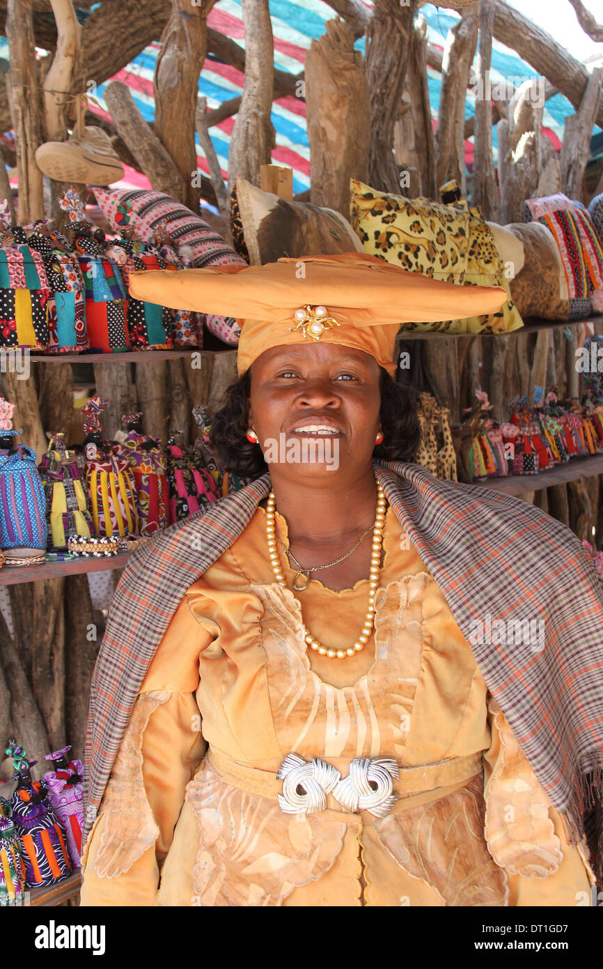 Herero woman in traditional German colonial  dress and   cow-horn hat in front of her souvenir dolls stall ,Namibia.Africa Stock Photo