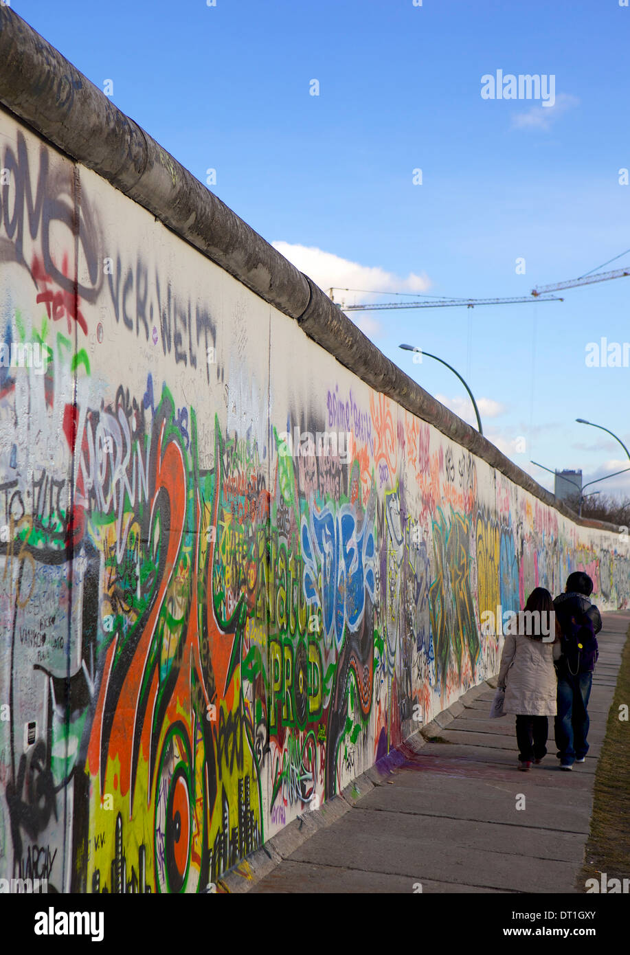 Couple walking along the East Side Gallery Berlin Wall mural, Berlin, Germany, Europe Stock Photo