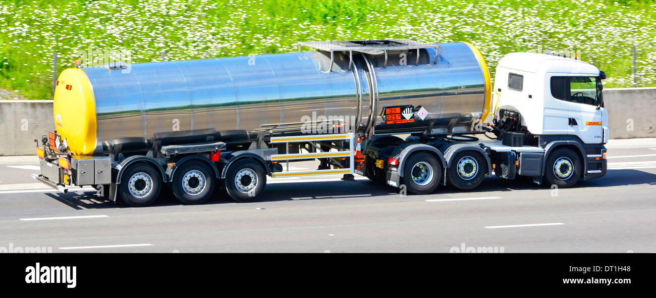 Shiny DHL tanker trailer behind a DHL Scania truck driving along motorway includes raised axle and Hazchem warning plates Stock Photo
