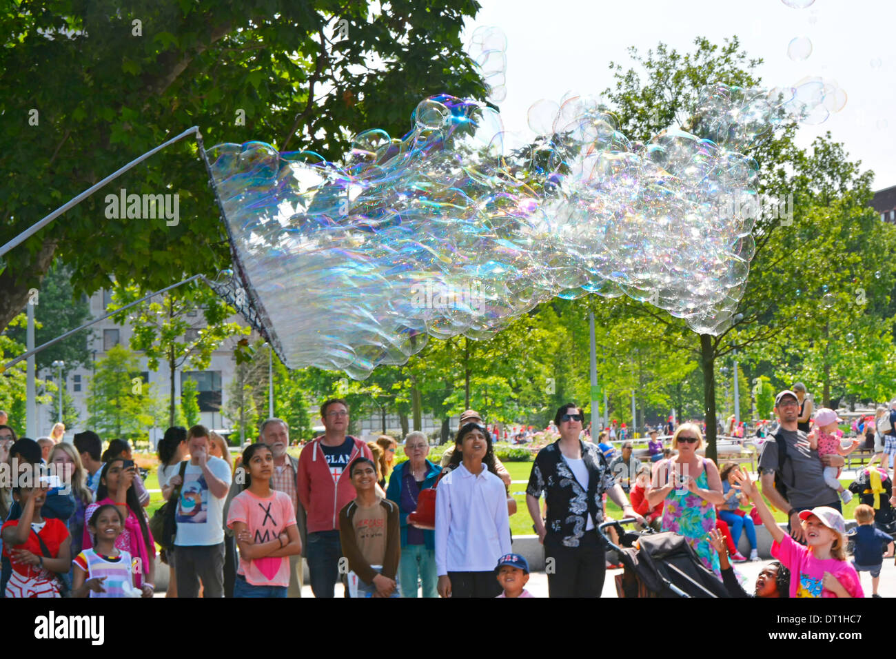 Families enjoying a demonstration of big bubble creations using a large net and cord wand on two poles Stock Photo