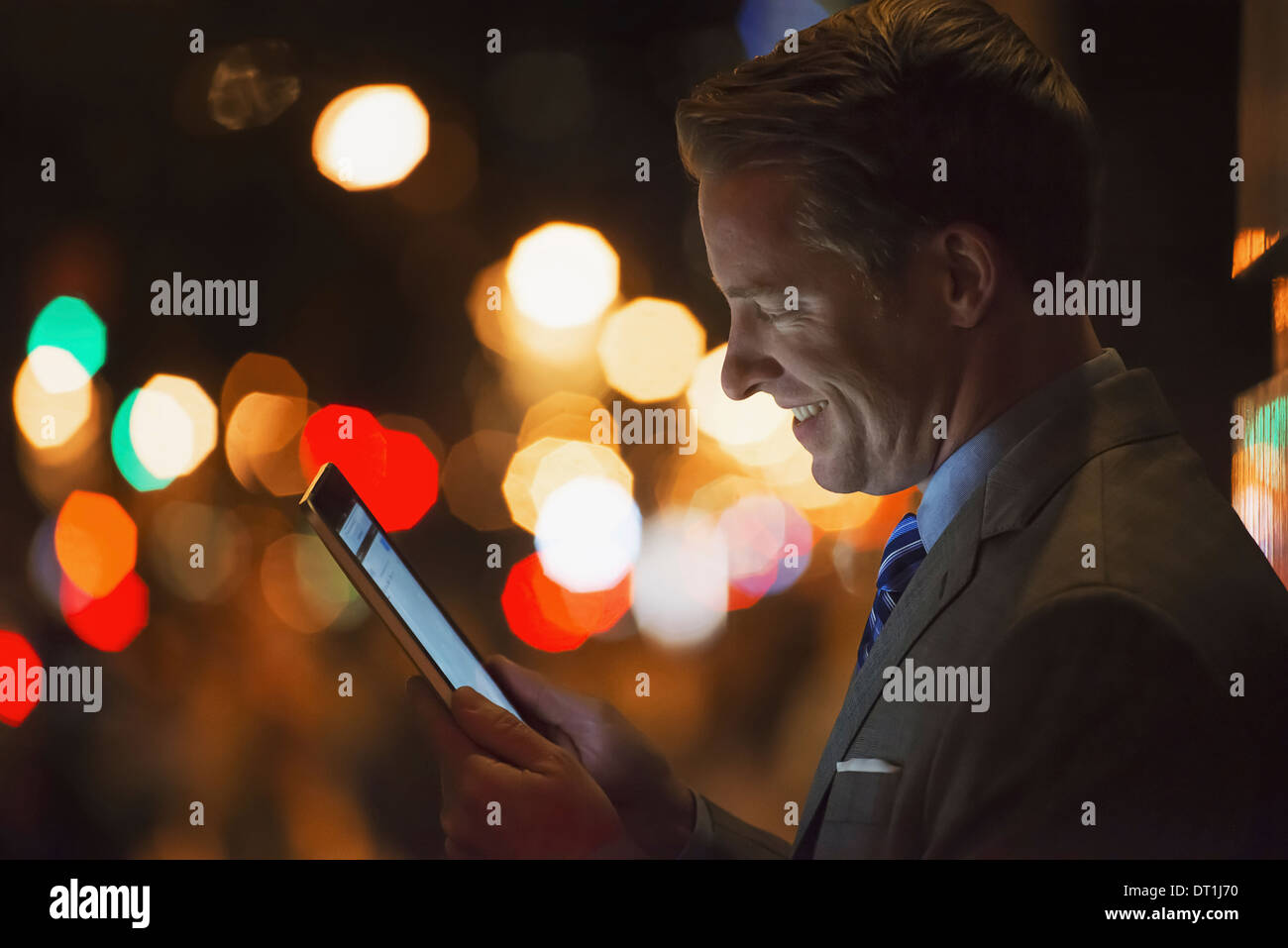 A man in a city at night looking at a computer tablet Stock Photo