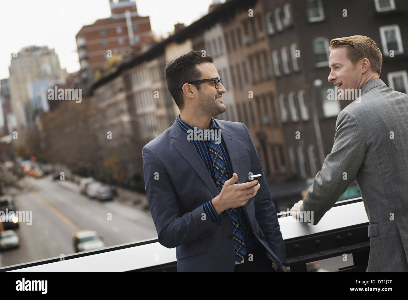 Two men standing talking on an elevated walkway above a city road Stock Photo