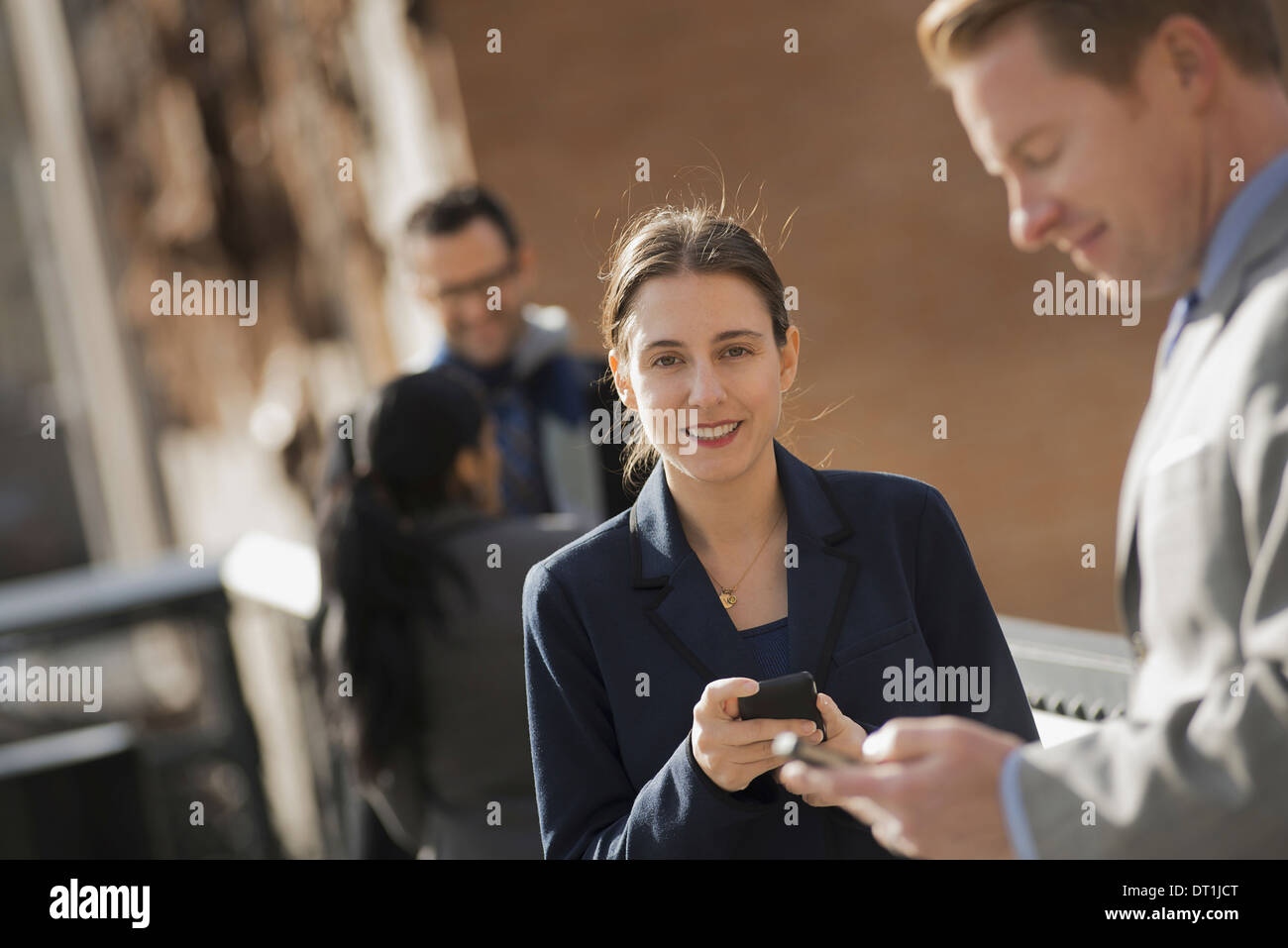 Three people standing on the sidewalk in the city checking their phones Two men and a woman Stock Photo