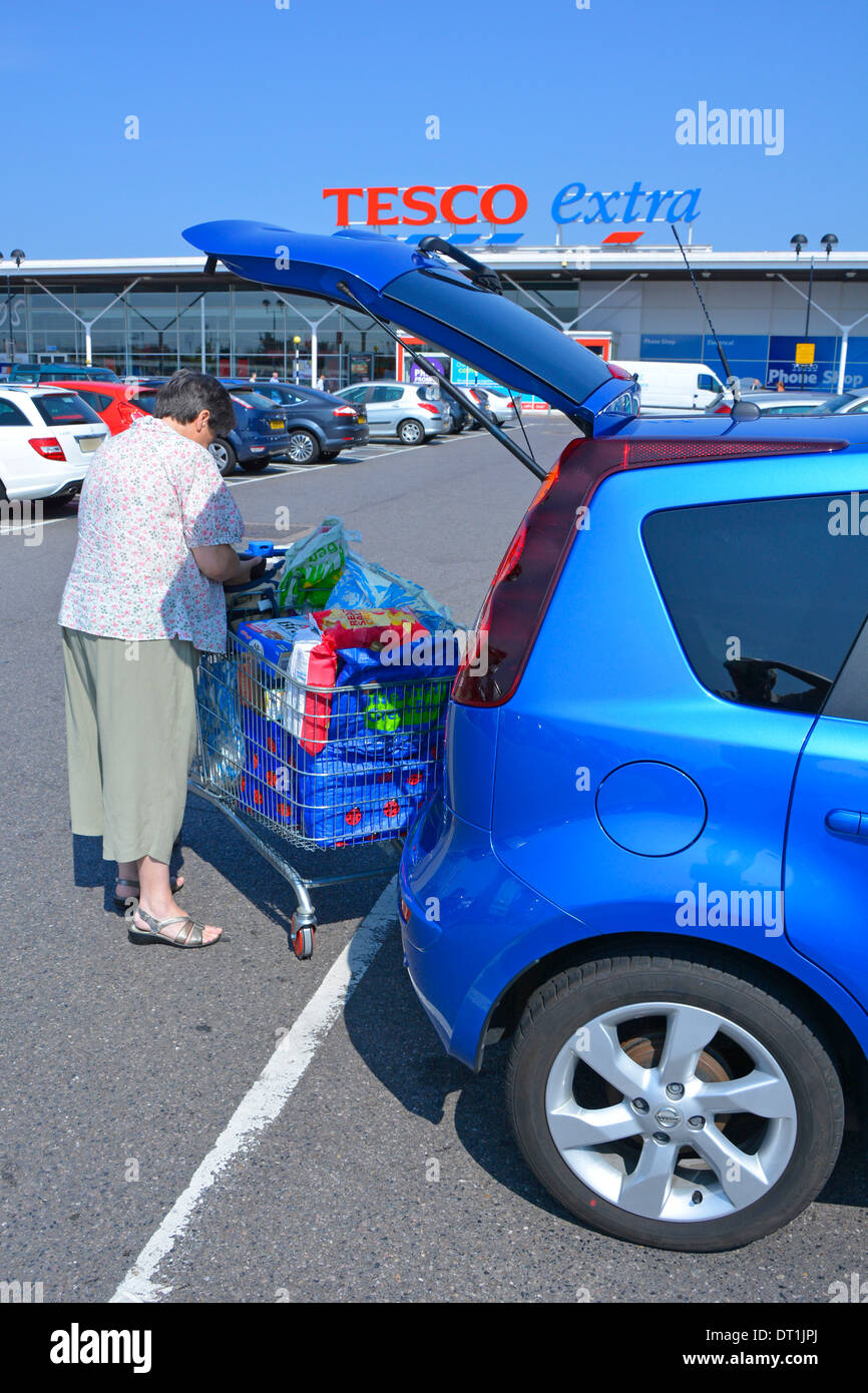 Tesco Extra supermarket store free car park and mature woman loading food shopping into hatchback car Stock Photo