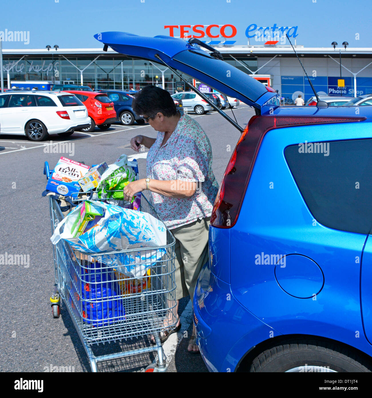 Tesco Extra supermarket store free car park and mature woman loading food shopping into hatchback car Stock Photo