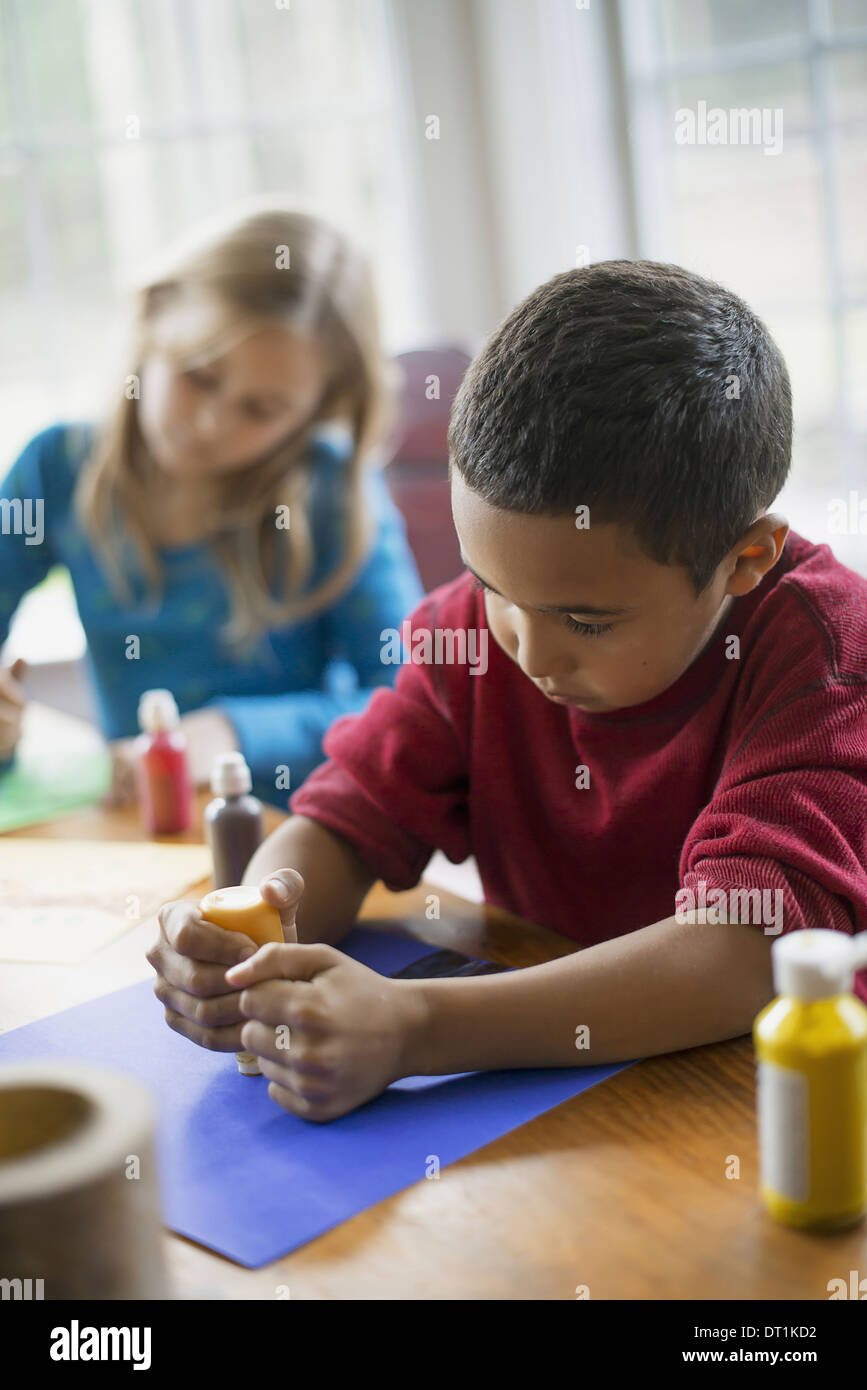 Children in a family home Two children sitting at the table using paint and paper to create decorations Stock Photo