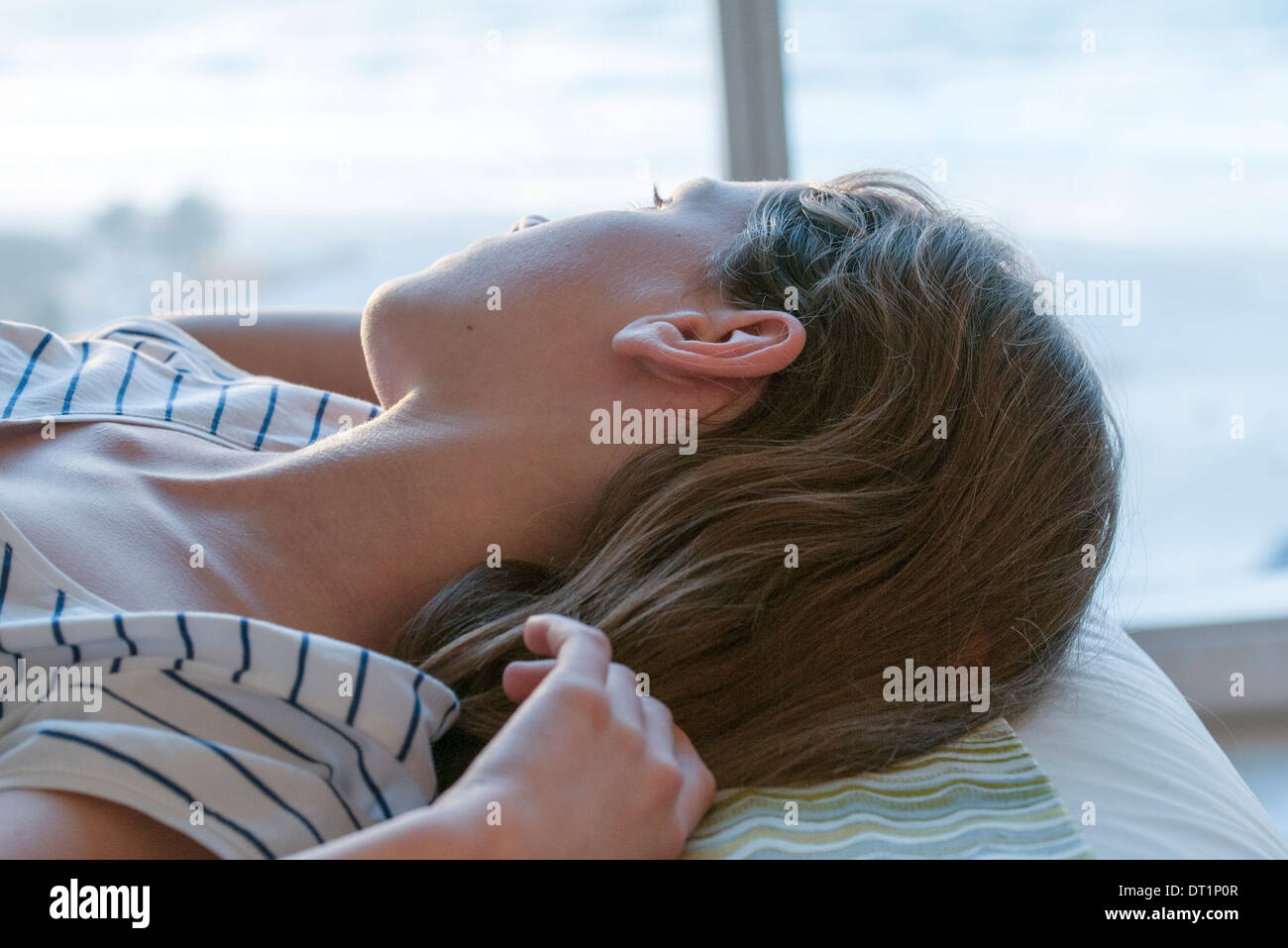 Girl lying on back, looking out window Stock Photo