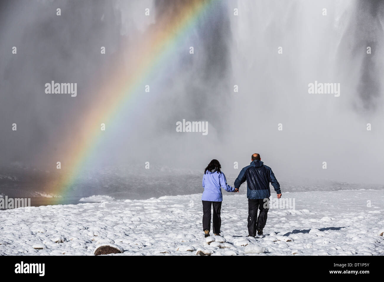 Rainbow over Skogafoss Waterfall in the Winter, Iceland Couple enjoying being close to the waterfall with a beautiful rainbow. Stock Photo