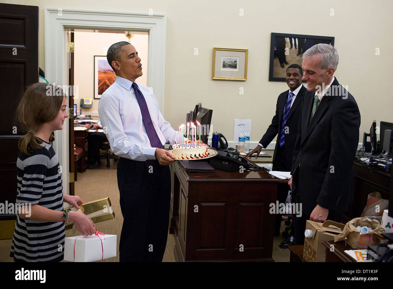 US President Barack Obama accompanied by Chief of Staff Denis McDonough's daughter, carries a birthday cake to surprise McDonough in the Chief of Staff's West Wing office December 2, 2013 in Washington, DC. Stock Photo