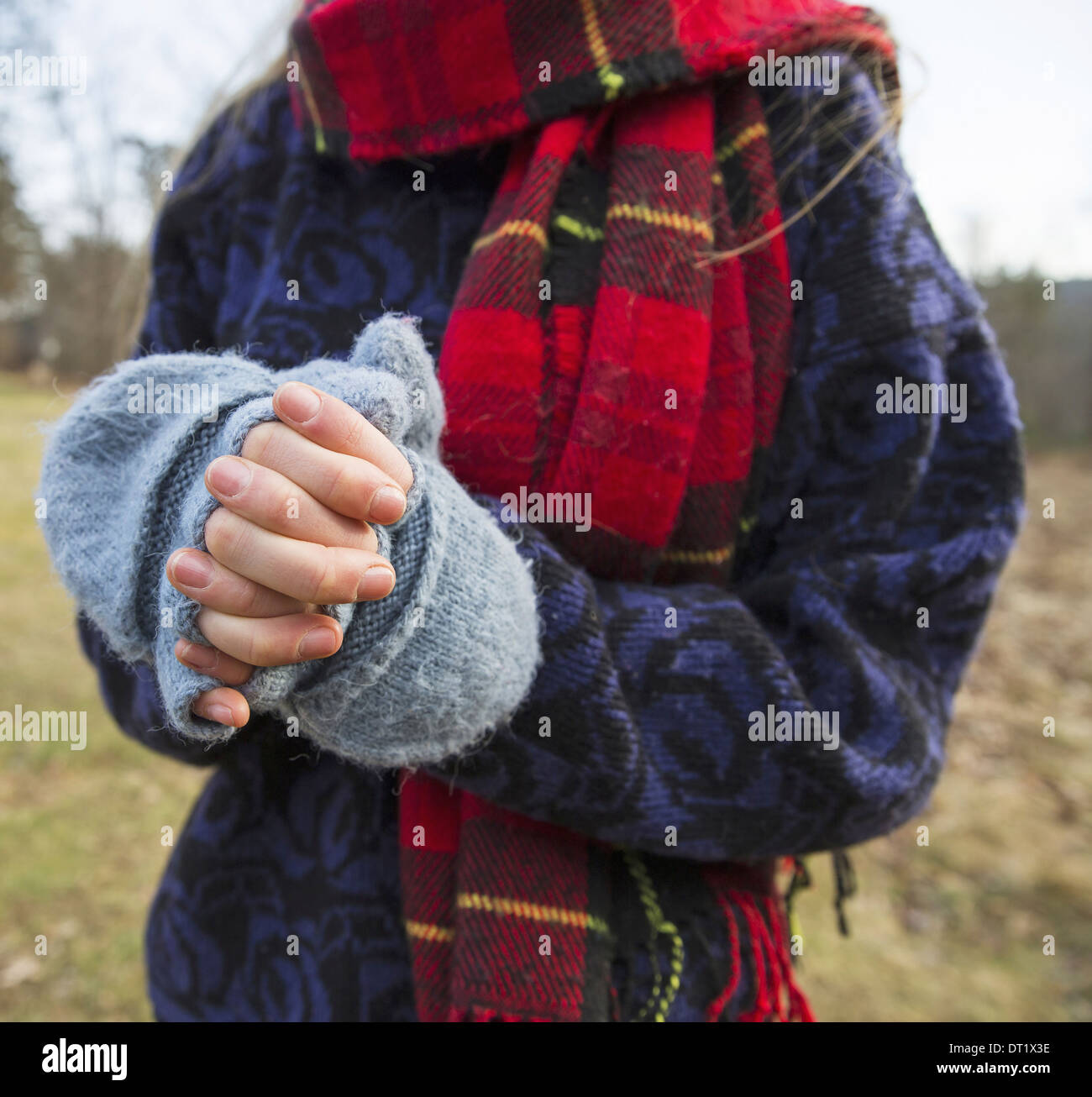 A woman in a tartan scarf and knitted woollen mitts keeping her hands warm in cold weather Stock Photo