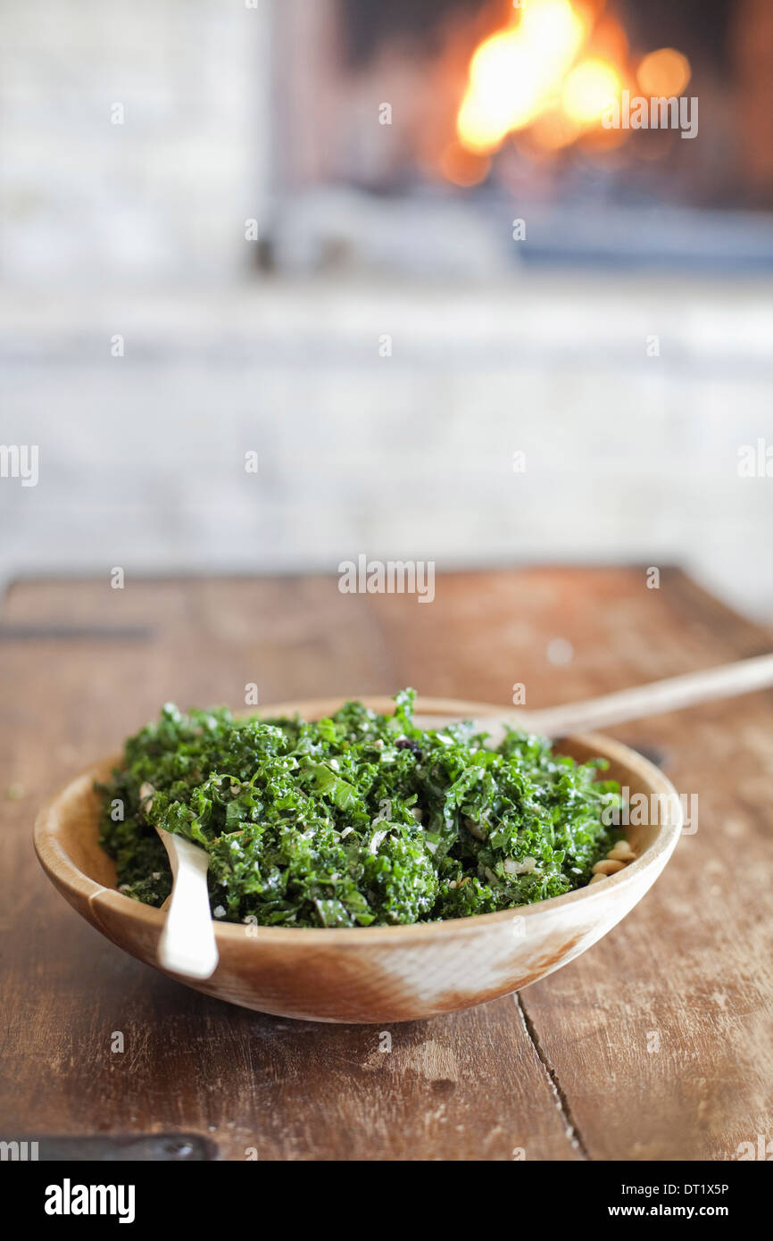 A tabletop with a log fire in the background Green leafy salad in a wooden bowl Stock Photo