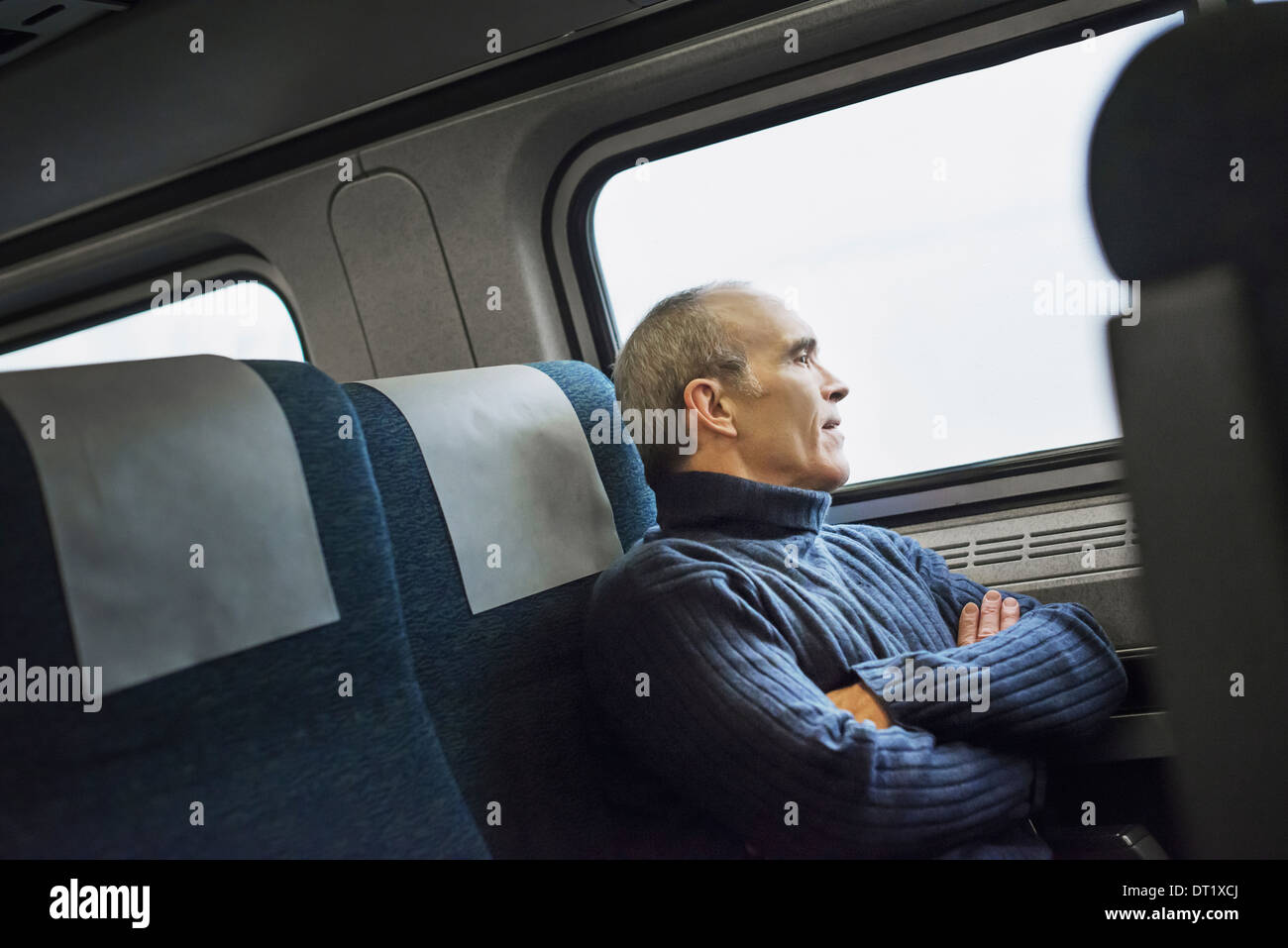 A mature man sitting in a window seat on a train journey looking out into the distance Stock Photo