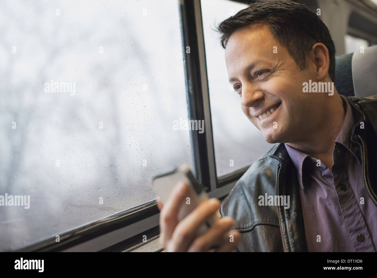 A mature man sitting at a window seat on a train holding his mobile phone Smiling and looking in the distance Stock Photo