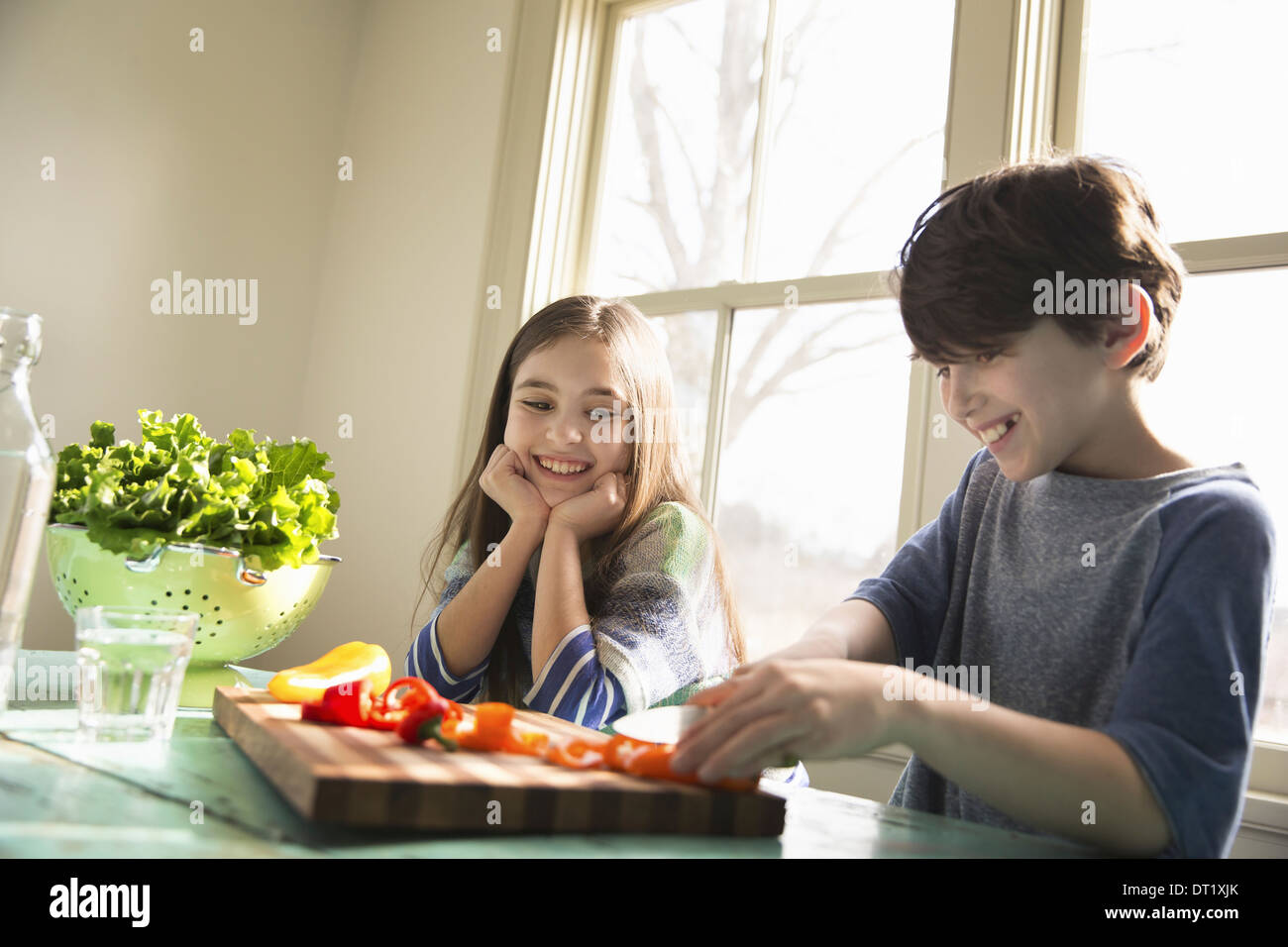 Two children sitting at a table A boy using a knife and chopping bell peppers on a board Stock Photo