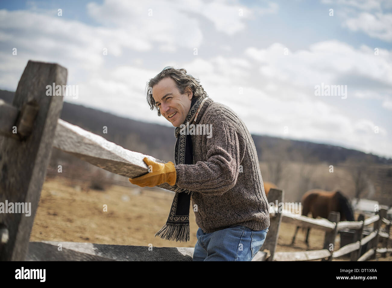 A man fixing a post and rail fence around a horse paddock Stock Photo