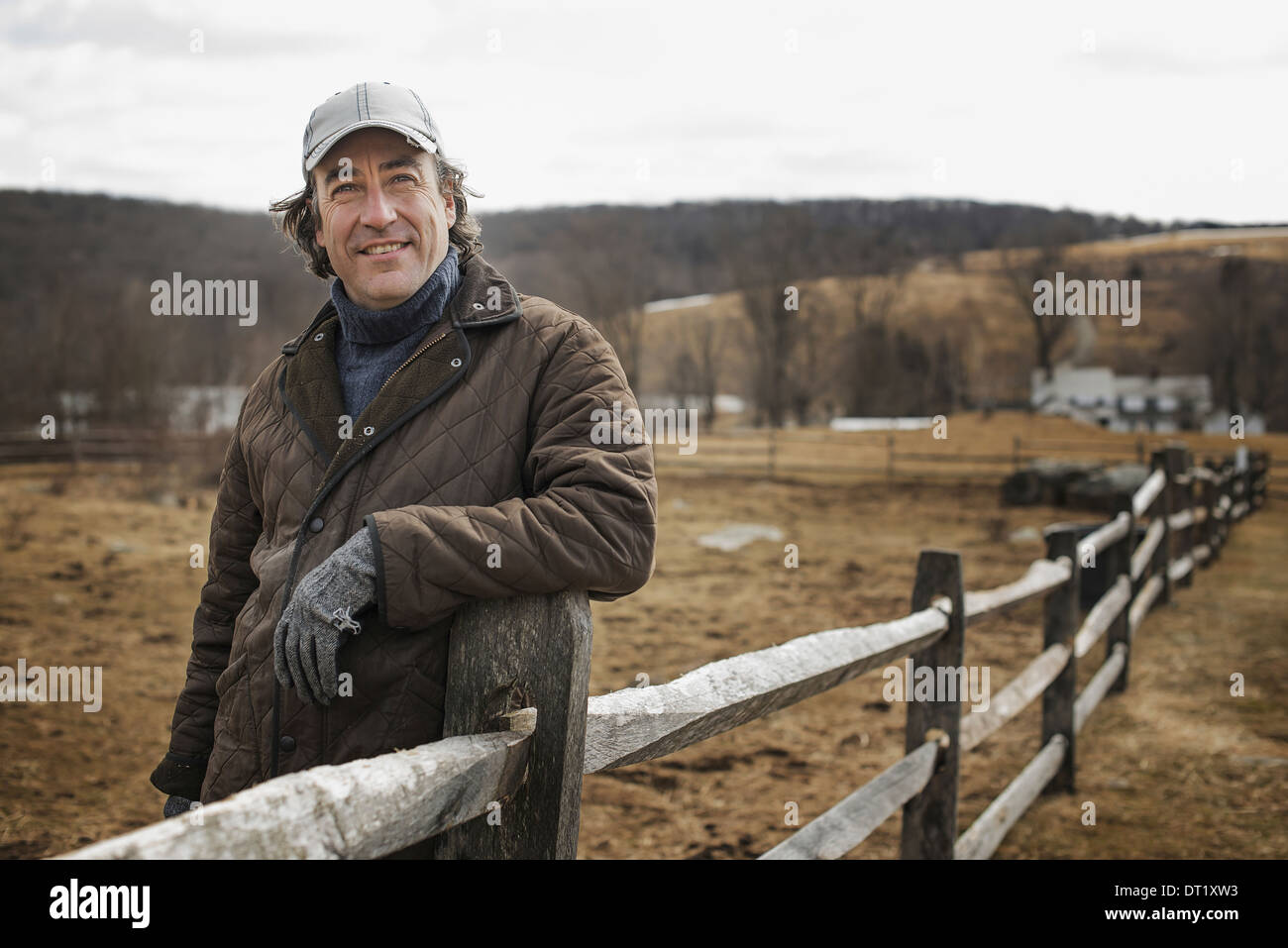 A man leaning against a post and rail fence on a farm in winter Stock Photo