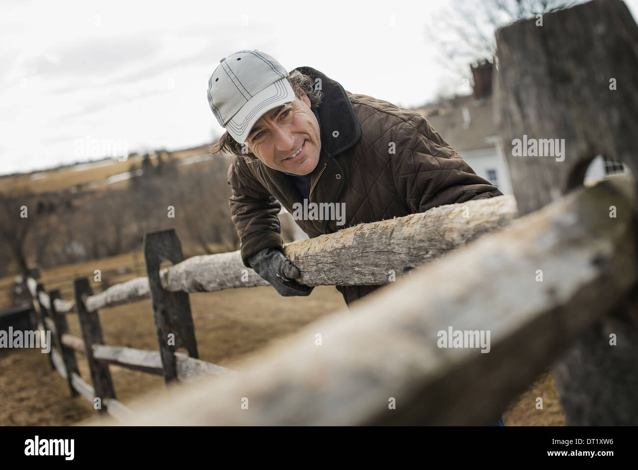A man leaning against a post and rail fence on a farm in winter Stock Photo