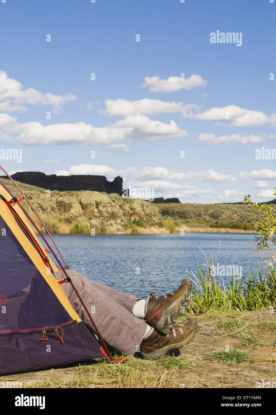 A small tent pitched by the shores of the Sun Lakes in Sun Lakes State Park A man's feet in loafers sticking out Stock Photo