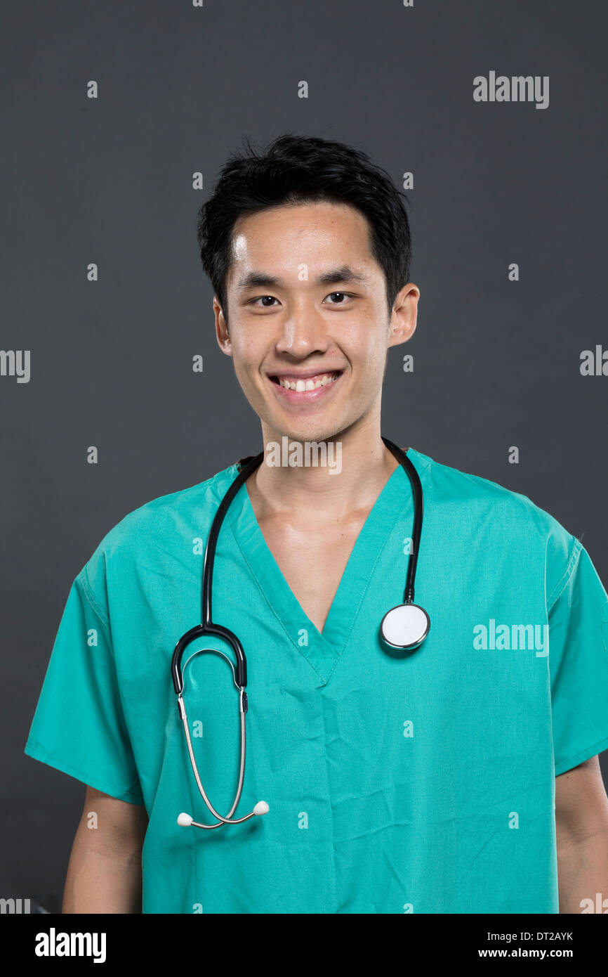 Portrait of a Male Asian doctor wearing Green Scrubs. Dark Grey background. Stock Photo
