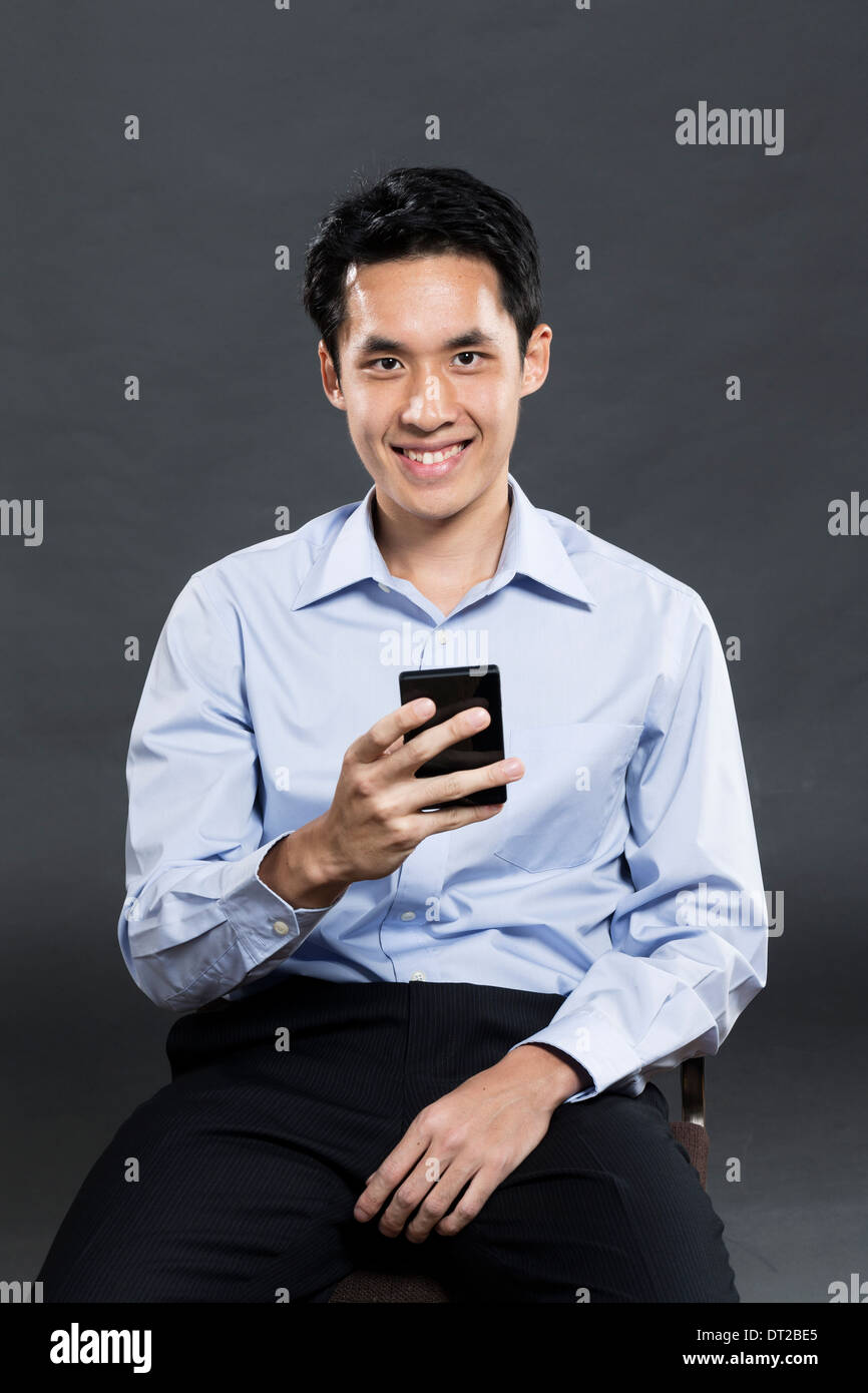 Portrait of a stylish Asian business man using a smart phone. Dark grey background Stock Photo