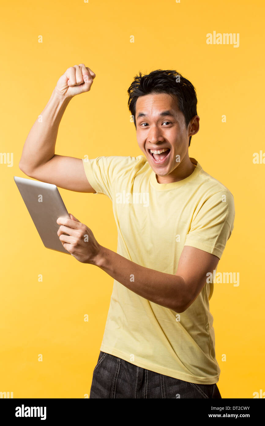 Cheerful Asian man celebrating with his arm up. In front of yellow background Stock Photo