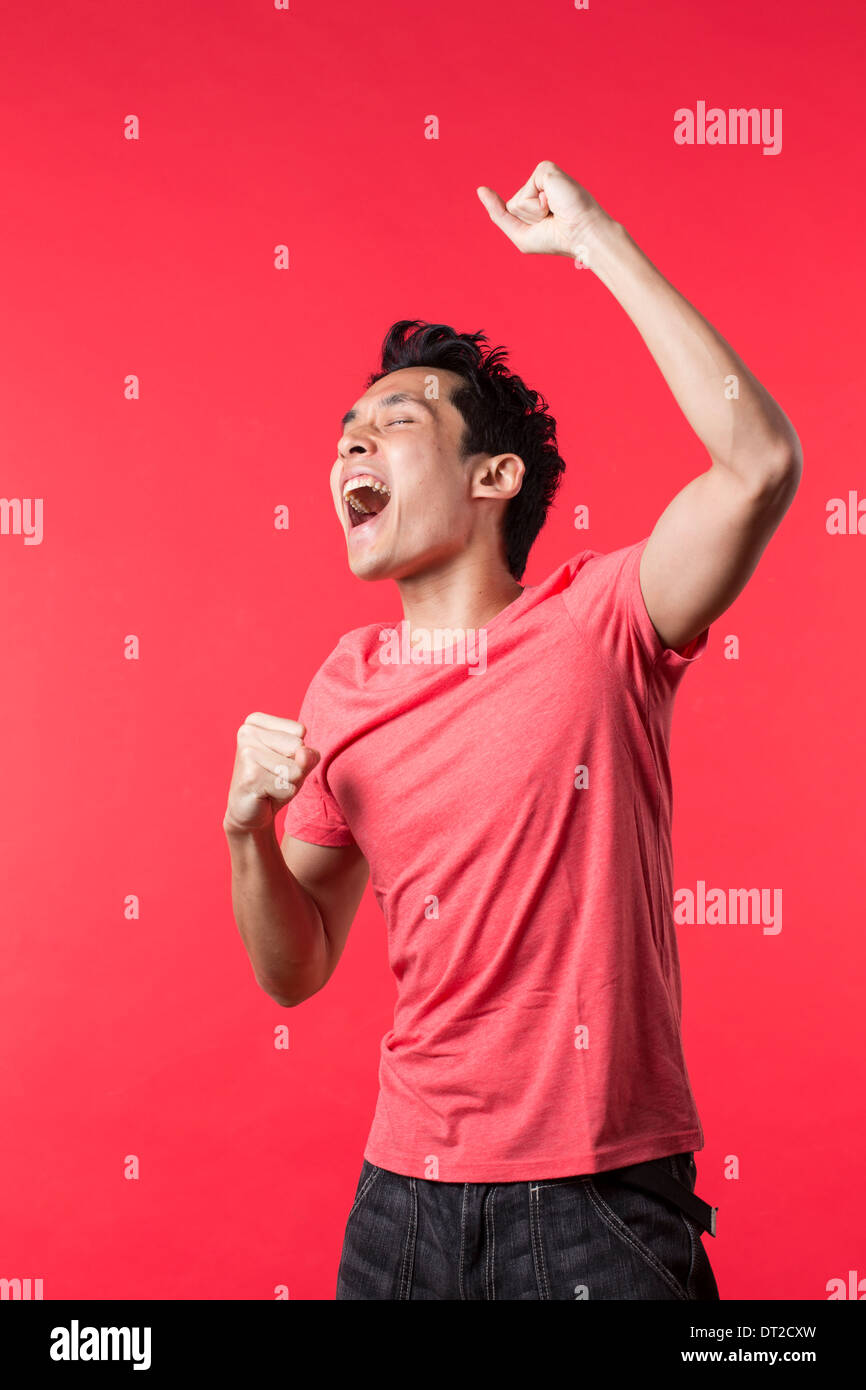 Cheerful Asian man celebrating with his arm up. In front of Red background Stock Photo