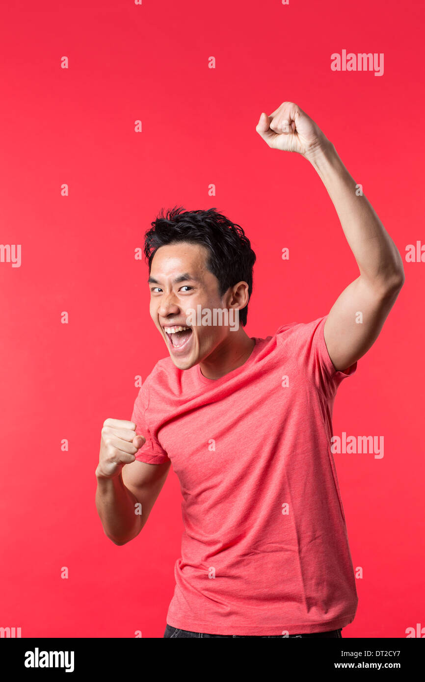 Cheerful Asian man celebrating with his arm up. In front of Red background Stock Photo