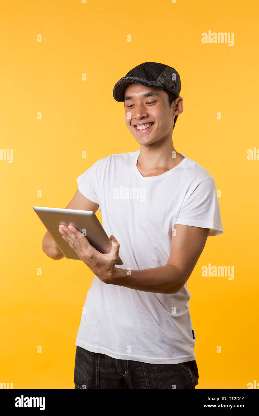 Cheerful Asian man using a tablet PC. In front of Yellow background. Stock Photo