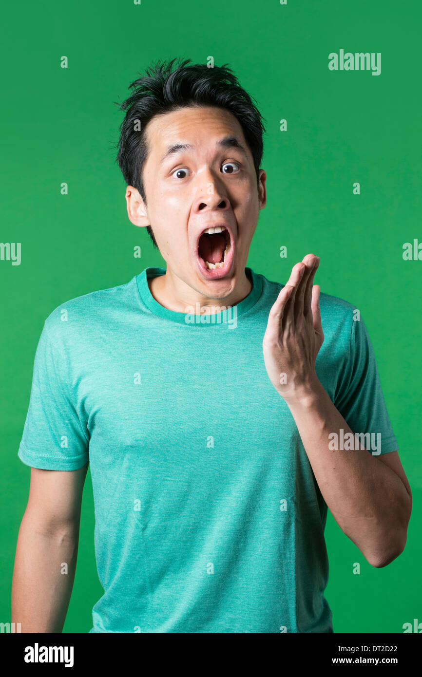 Surprised and amazed looking Asian man standing against green background. Stock Photo