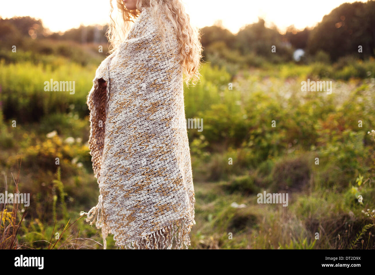 Young woman covered with blanket standing on meadow, mid section Stock Photo