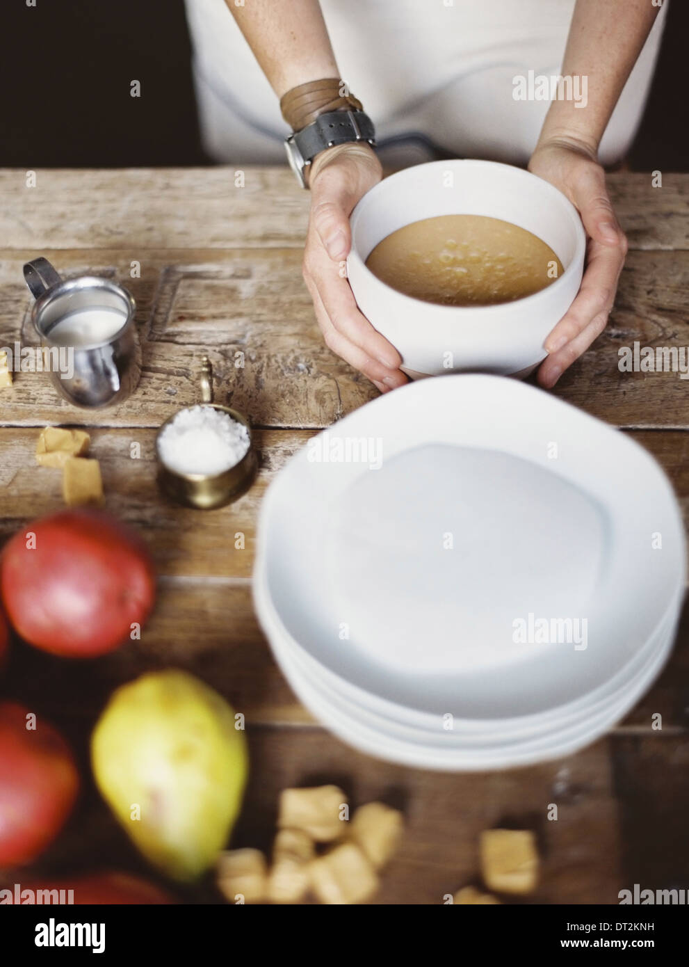 A domestic kitchen tabletop A stack of white plates and fresh pears and a stack of sugar cubes A bowl of fudge sauce Stock Photo