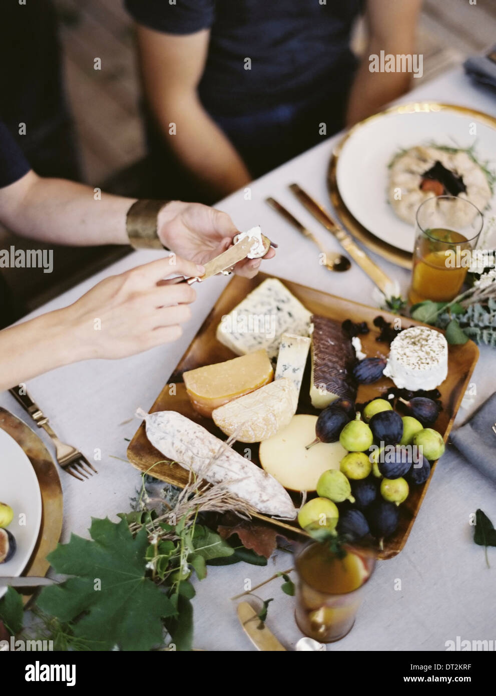 A table white cloth place settings An organic cheese board with soft and hard cheeses and figs Two people sitting at the table Stock Photo