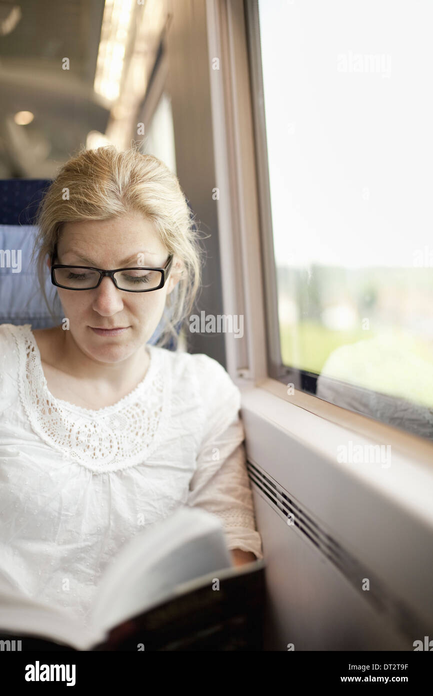 A woman sitting by a train window reading a book Stock Photo