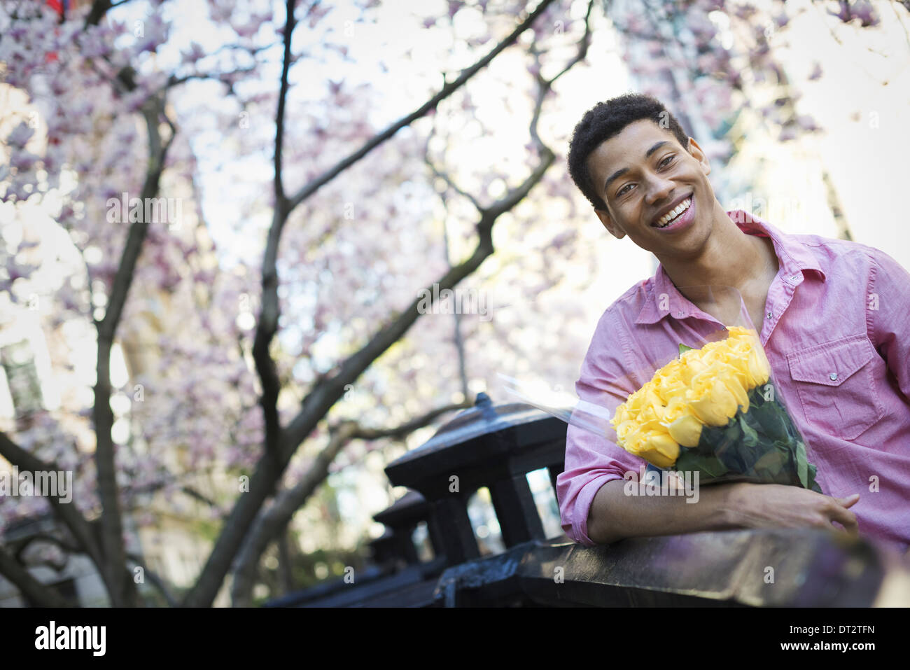 A young man in the park in spring holding a bunch of yellow roses Stock Photo